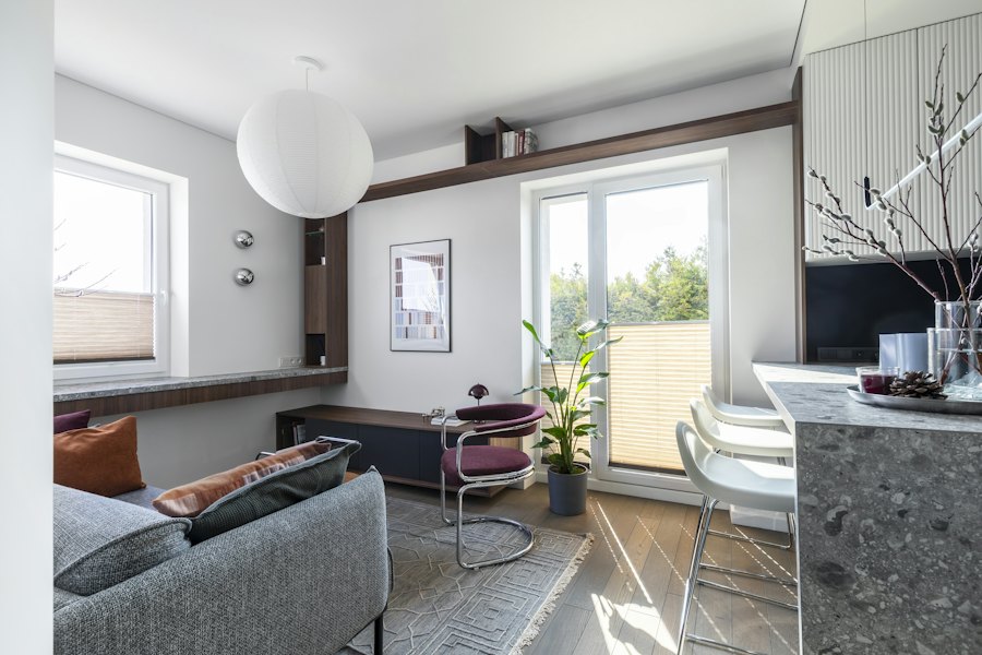 Sala de um apartamento claro com luminária globo, poltrona bordô, marcenaria em nogueira e porta de vidro para a varanda.