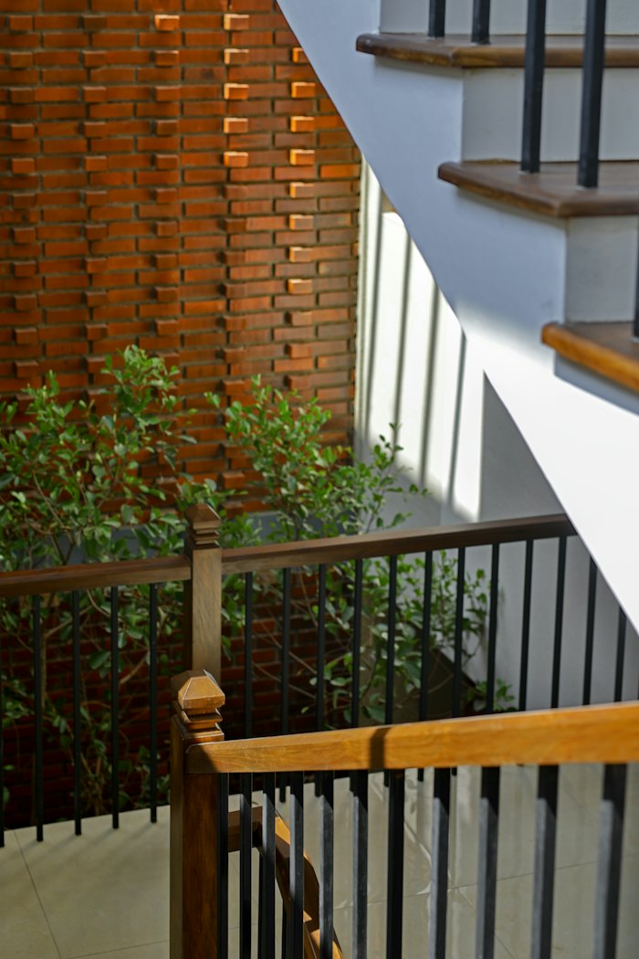 Escada com guarda-corpo de madeira ao lado de um jardim interno, com parede de tijolo vazado deixando a luz entrar.