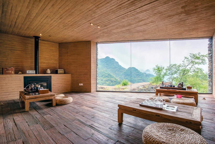 A sala com lareira e a janela de canto a canto que enquadra as montanhas.